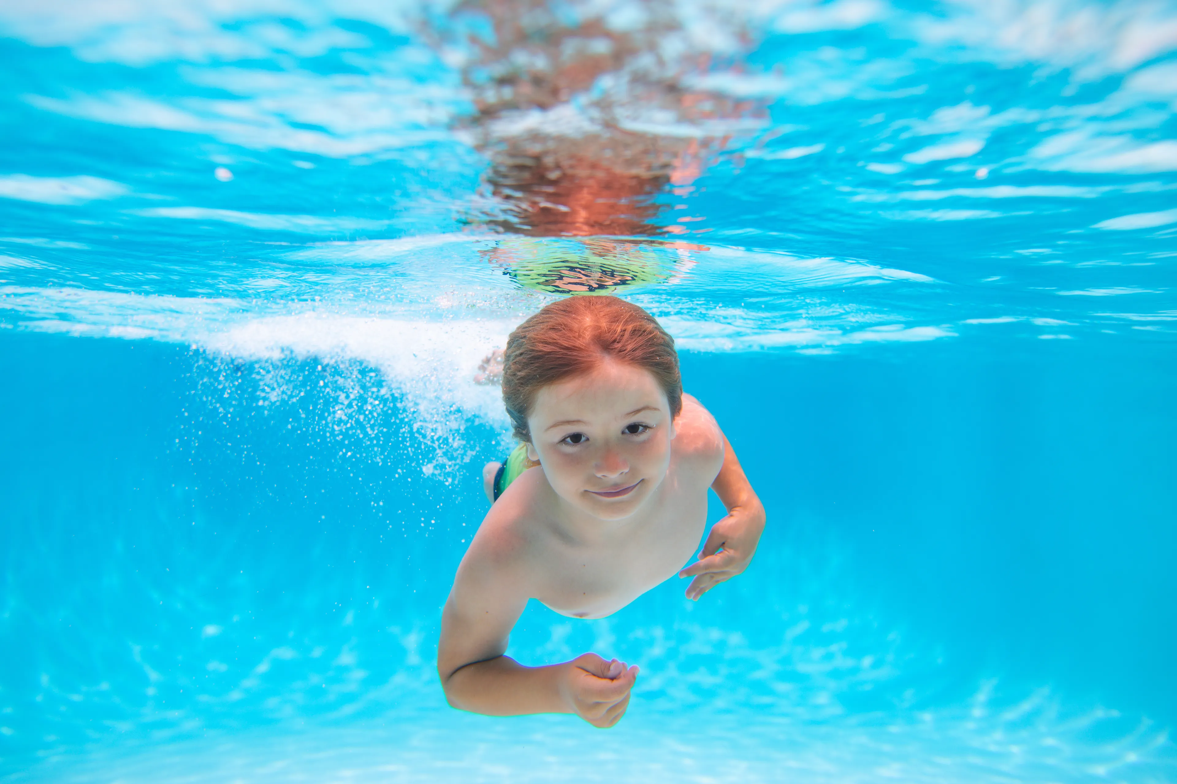 Das Bild zeigt einen Jungen im Wasser eines Schwimmbecken der frontal auf die Kamera gerade zutaucht.